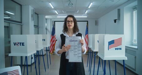 American female voter or polling officer speaks on camera, shows paper ballot, calls for voting....
