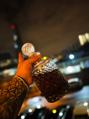 An urban night out captured through a crystal-clear whiskey decanter, elegantly held up against a...
