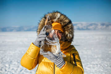 Happy woman wearing winter yellow jacket holding piece of transparent crushed ice cubes over her...