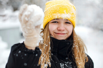 Portrait of funny happy teenage girl in yellow knitted hat plaing with snow outdoors - obrazy, fototapety, plakaty