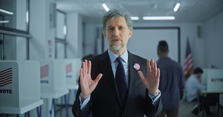 Portrait of man, United States of America elections voter. Businessman with badge speaks on camera and calls for voting in modern polling station. Background with voting booths. Concept of civic duty.