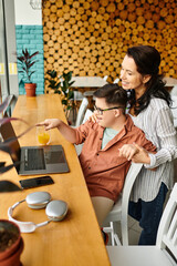 jolly inclusive preteen boy with Down syndrome sitting in front of laptop and phone next to his mom