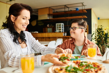 cheerful mother eating pizza and drinking juice with her inclusive cute son with Down syndrome