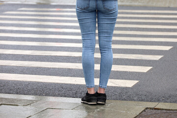 Female legs against the pedestrian crossing. Woman in jeans waiting the street at a crosswalk, road safety