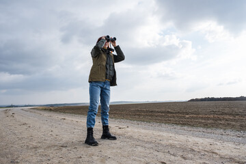 female ornithologist birdman or explorer watches birds with binoculars against a background of a stormy sky - 788369636