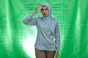 young Asian woman wearing hijab and blouse looking dizzy and having headache on green background
