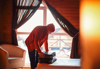 Stylish hipster traveller man in red hat in wooden house packing suitcase