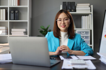 Asian businesswoman working on documents with laptop in office.