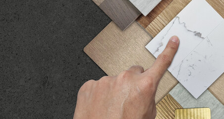 interior architect's hand chooses material samples including brushed gold stainless, bronze laminated, stone tile, wooden flooring tile, white marble quartz, veneer. table top view.