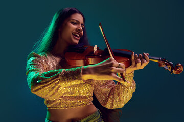 Happy young Indian woman, violin player in sparkling gold top, immersed in music in neon light against gradient background. Concept of art, music, hobby, classical music and modern lifestyle. Ad - obrazy, fototapety, plakaty
