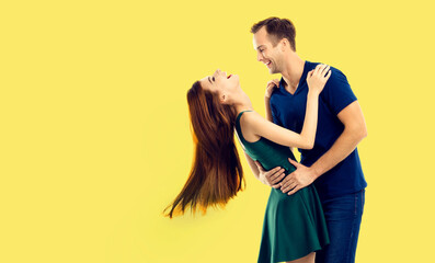 In love, relationship, dating, lovers, romantic concept - full body of hugging embracing dancing couple, look at each other. Portrait of happy young man and woman, isolated against yellow background. - obrazy, fototapety, plakaty