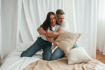 Soft pillows are in hands, playing. Young couple are together at home