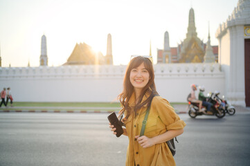 Traveler asian woman in her 30s stands bathed in the golden glow of sunset, embracing the freedom...