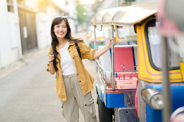 Young Asian woman backpack traveler standing a side of Tuk Tuk taxi on summer vacations at Bangkok,...