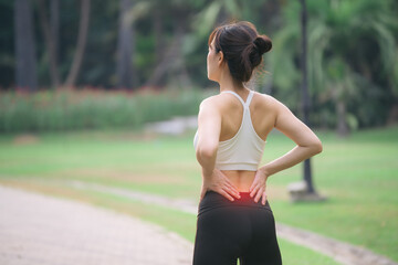 Back pain problem. woman jogger. 30s asian female wearing white sportswear holding her back with pain after running exercise in public park. - 788388276