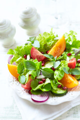 Salad with red and yellow Tomatoes and Pomegranate Seeds on bright wooden Background. Close up.