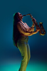 Side view photo of Indian woman, saxophonist performing solo in neon light against gradient...
