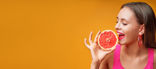 Beauty portrait of a lovely young woman with long hair standing over yellow background banner, showing slices of a grapefruit.