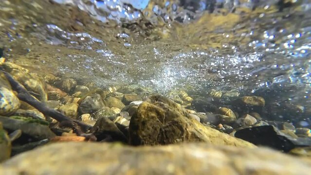 Unterwasservideo von einem Bach mit Steinen und Luftblasen im fließenden Wasser in Zeitlupe 