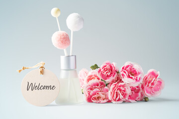 Fragrance diffuser with welcome tag and pink flowers on vintage blue background