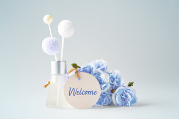 Welcome paper tag with fragrance diffuser and flowers on vintage blue background