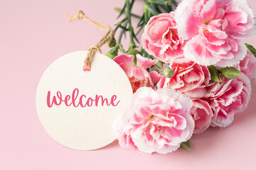 Welcome tag and carnation flowers on pink background