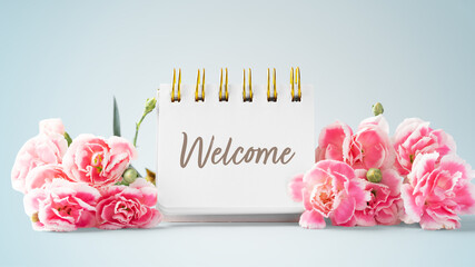 Welcome word on notepad and pink flowers on blue vintage background