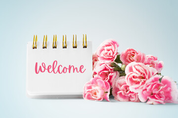 Welcome word on notebook and carnation flowers on blue vintage background
