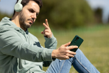 man listening to music with headphones while taking a selfie to send a photo on his mobile phone to...