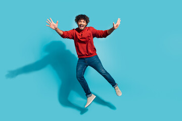 Fototapeta na wymiar Full length body size photo of overjoyed curly hair hispanic guy raised arms up having fun jumping isolated on blue color background