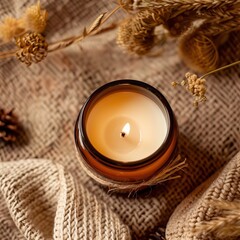A close-up image of a lit candle in a brown glass jar with a burlap background.