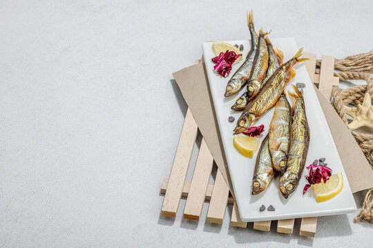 Smoked smelt with fresh lemon and herbs. Salted fish with marine decor. Trendy dish, sea rope