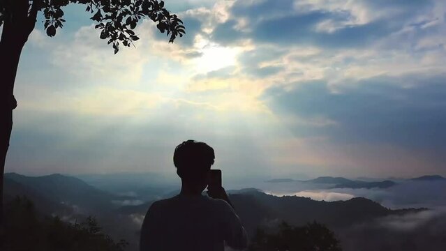 A person stands on a viewpoint and takes a video of the fog in Phu Bo Bit Forest Park, Loei Province, Thailand, and watches the sunrise. Miracles of nature hill standing shadow sunlight. - video