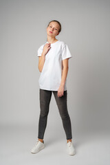Beautiful young girl posing in white T-shirt and jeans on gray background