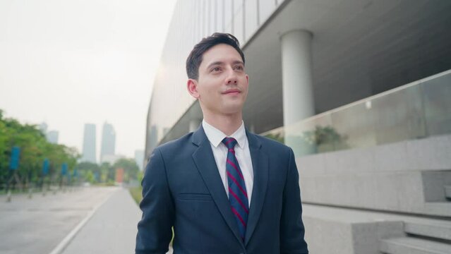 Young mix race light skin businessman in smart attire walking to work on the urban streetside with modern building exterior behind him, confident working person, business owner looking at time 