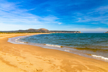 Las olas besan suavemente la Playa de la Estartit en la Costa Brava, con montañas al fondo bajo un cielo azul en la vibrante primavera. - obrazy, fototapety, plakaty