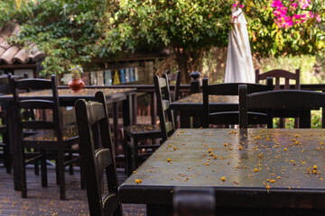 A patio with a few tables and chairs. The tables are covered in leaves and the chairs are empty