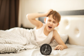 Kid boy teenager waking up yawning and stopping alarm clock in morning