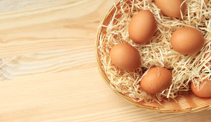 Chicken eggs in a wicker basket, top view. Eggs on a wooden background. Fresh raw eggs. Brown chicken eggs in a basket on a wooden table. Space for text - obrazy, fototapety, plakaty