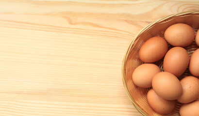 Chicken eggs in a wicker basket, top view. Eggs on a wooden background. Fresh raw eggs. Brown chicken eggs in a basket on a wooden table. Space for text