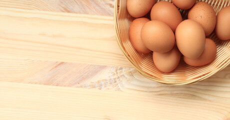 Chicken eggs in a wicker basket, top view. Eggs on a wooden background. Fresh raw eggs. Brown chicken eggs in a basket on a wooden table. Space for text - obrazy, fototapety, plakaty