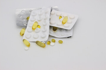 A scattering of multicolored medical pills, their packaging on a light background. - obrazy, fototapety, plakaty
