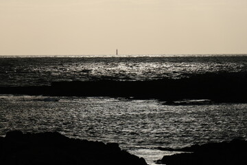 A small lighthouse on the horizon and a silver reflection on the Atlantic Ocean. Le Croisic, France...
