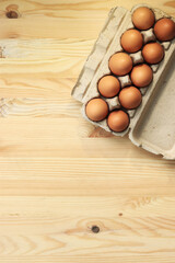 Chicken eggs in a cardboard box, top view. Eggs on a wooden background. Ten fresh raw eggs. Brown chicken eggs in a recycled cardboard tray on a wooden table