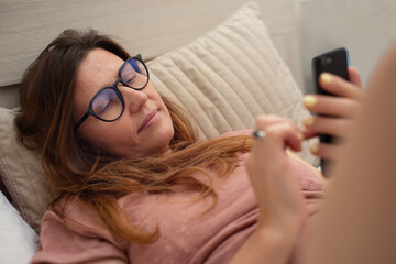 A woman wearing large reading glasses looks at her mobile phone screen and types a message while...