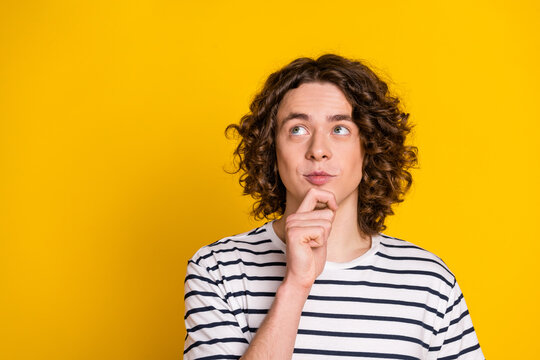Portrait of young funny guy curly hair touch chin looking empty space deep thinking find solution isolated on yellow color background