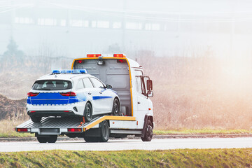 Roadside assistance. Tow truck transporting a broken police officer car on a highway. Flatbed...