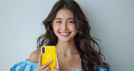 A young woman with long dark hair, smiling and holding a yellow smartphone, wearing a blue blouse.