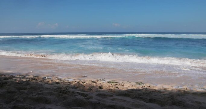 Sandy beach on sunny day with blue ocean waves in tropics