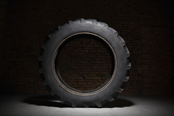 Old used tractor wheel on black background. Tyres shop. Front view.